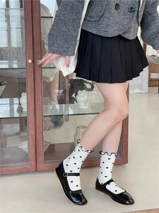 Close-up of white crew socks with black heart patterns and ruffled edges with Mary Janes