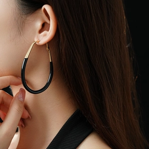 Close-up of a model wearing large black enamel oval earrings with gold metal accents