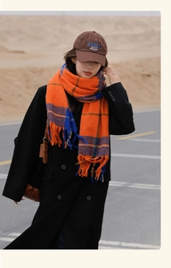 Outdoor shot of an orange and blue plaid tassel scarf paired with a black trench coat