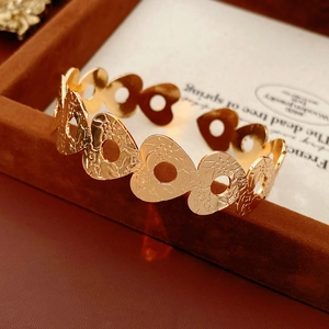 Detail of gold open bangle featuring heart cut-outs and floral texture on velvet