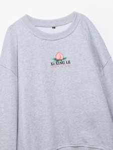 Détail à plat d'un sweat-shirt gris clair avec broderie graphique de pêche élégante