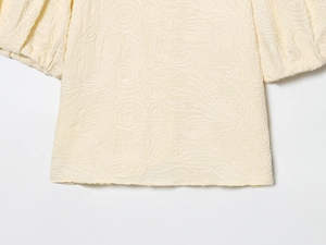 Détail du chemisier beige avec broderie en relief et manches bouffantes de style lanterne