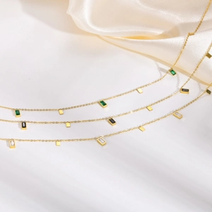 Minimalist gold titanium necklaces with emerald, black, and white zircon pendants on silk