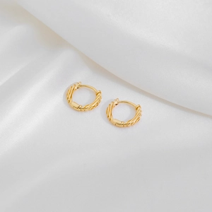 Detail of gold-colored twisted rope huggie earrings on white silk fabric background