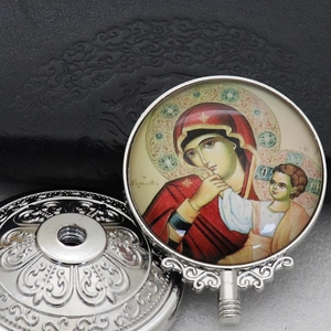 Macro shot of silver metal base with ornate reliefs and Virgin Mary glass dome pendant