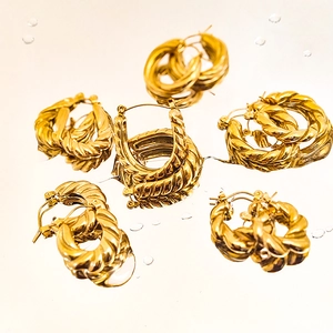 Detail of gold-plated stainless steel hoop earrings with twisted texture on a mirror base