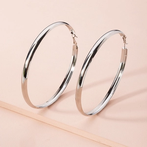 Macro view of polished silver large hoop earrings with secure pin closures on pink background
