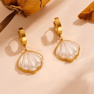 Macro shot of gold shell earrings with pearl white pendants on textured background