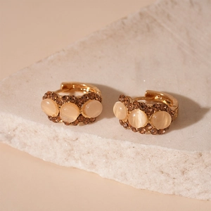Vue latérale macro de créoles dorées avec pierres œil de chat beige et strass champagne