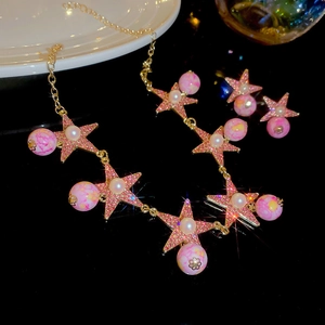 Detail of pink star jewelry set with gold chains and pearl accents on black reflective surface