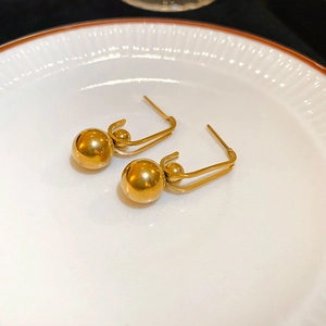 Detail of minimalist gold U-shaped earrings with polished metal spheres on a ceramic plate