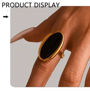 Detail of a large oval black enamel ring with gold-plated stainless steel band on a finger