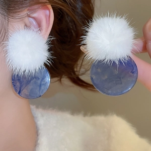 Detail of earring with white fuzzy pom pom and blue marble acrylic circular pendant