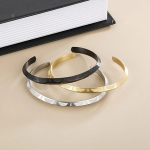 Macro detail of three-piece C-shaped steel bracelets with engraved textures in black, gold, and silver