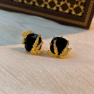 Detailed view of gold-plated leaf earrings featuring large black gemstone on white fabric