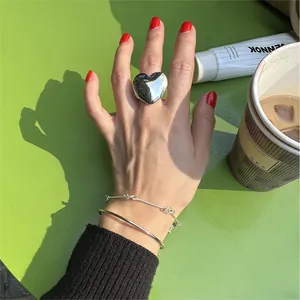 Macro detail of oversized silver heart ring and layered bangles on green background