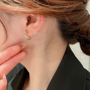 Macro detail of C-shaped gold-plated metal earring with white pearl backing on model