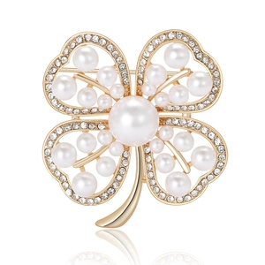Elegant gold clover brooch with white pearls and sparkling crystals on white background