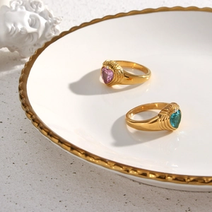 Close-up of 18K gold plated rings with pink and blue heart zircons on white ceramic tray