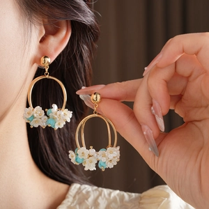 Detail of floral earrings with white petals and blue beads worn for vacation style