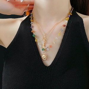 Detail of a triple-layer gold necklace featuring sun, moon, and star pendants with colored stones
