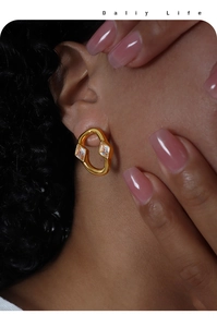 Close-up of golden irregular hoop earring with sparkling diamond-shaped zircon stones