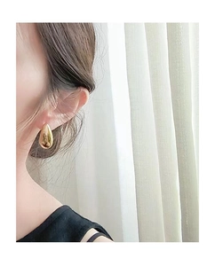 Close-up of model wearing large gold waterdrop earrings with a polished metallic finish