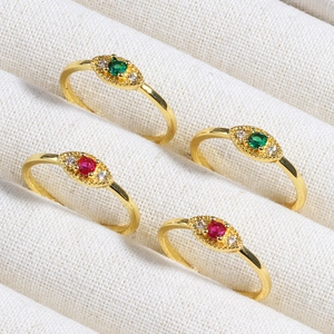 Detailed view of gold evil eye rings with emerald and ruby zircon stones on white fabric