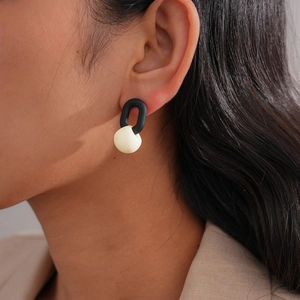 Detail of minimalist black matte oval and white spherical drop earring on ear