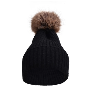 Dettaglio del berretto in maglia nera con un soffice pompon in finta pelliccia marrone