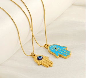 Detail of Hamsa Hand and Evil Eye gold necklace with blue enamel on silk background