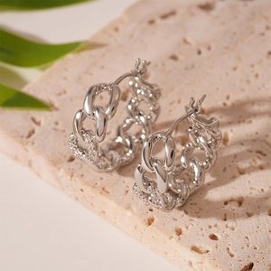 Close-up of silver chain link hoop earrings with zircon pavé on beige stone base