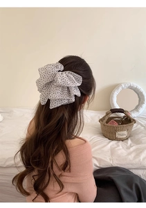 Close-up of a white polka dot chiffon bow hair clip worn on long wavy hair in a bedroom
