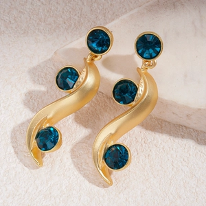 Detail of gold-plated S-shape earrings with inlaid blue circular crystals on stone