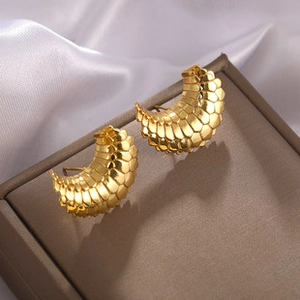 Detail of gold C-shaped earrings with unique scale texture on premium white satin