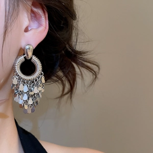 Close-up of silver geometric hoop earrings with metallic teardrop sequin tassels