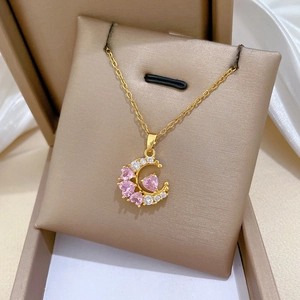 Detail view of a gold moon necklace with pink heart and clear zircon in a jewelry box
