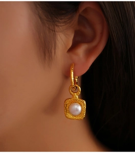 Close-up of golden vintage textured square earrings featuring a white freshwater pearl