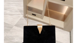 Detail of elegant black velvet evening bag featuring gold leaf clasp and metal chain strap