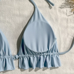 Detail of light blue bikini top with halter neck ties and ruffled edge on fabric