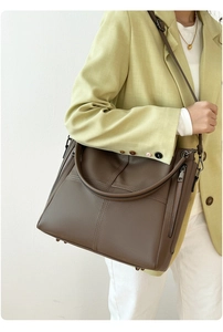 Fashion model wearing a dark brown leather tote bag with embossed letter texture