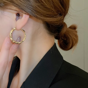 Close-up of golden geometric hoop earrings with textured finish worn by a model