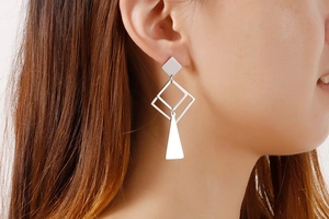 Close-up of long silver geometric earrings featuring rhombus and square dangles