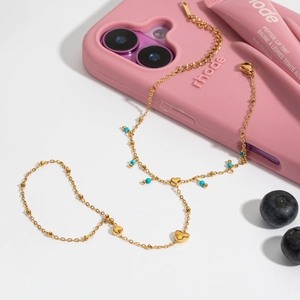 Detail of 18K gold stainless steel bracelet with blue beads and heart charms on phone