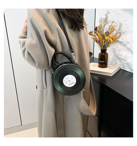 Detail view of a dark green vinyl record shaped PU leather crossbody bag on a model