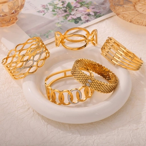 Five gold hollow-out titanium steel bangles with zircon accents on ceramic tray