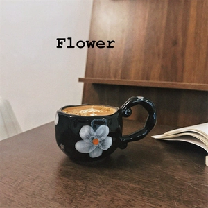 Detail of irregular black ceramic mug with hand-painted white flowers and latte art