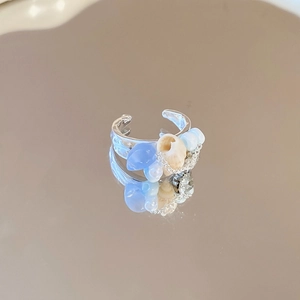 Detail of silver shell ring with blue beads and chain element on reflective surface