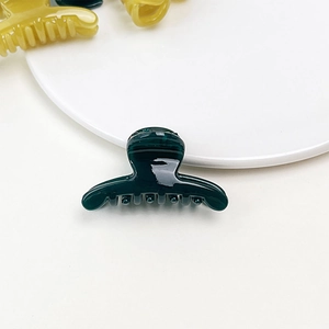 Macro shot of dark green jelly texture small hair claw clip on a white decorative plate