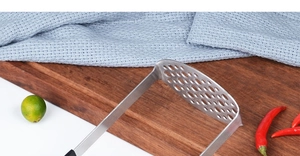Presse-purée en acier inoxydable avec poignée noire sur planche en bois dans une cuisine